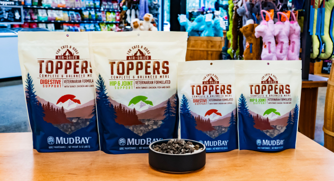 lineup of Mud Bay Air Dried Toppers with both sizes of bags and bowl of toppers over kibble
